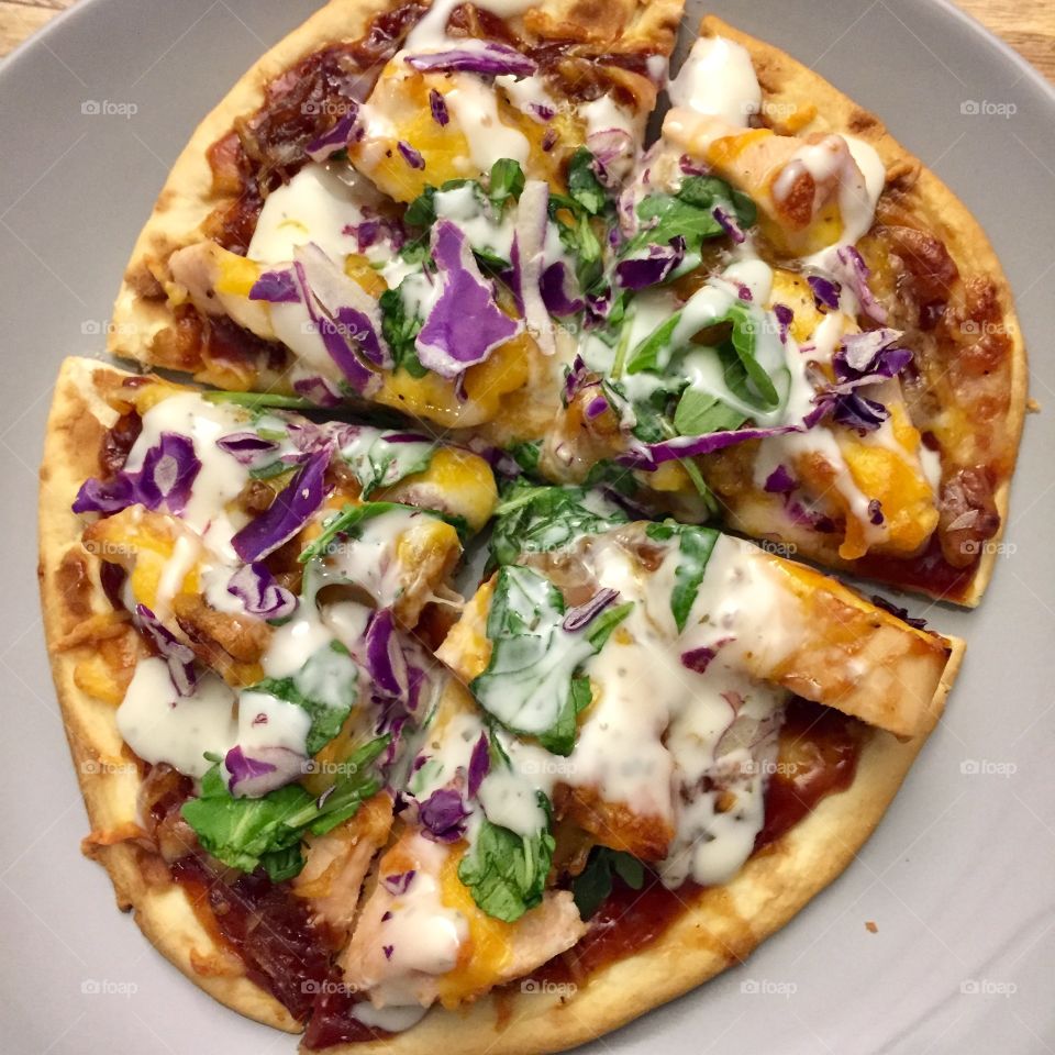 BBQ chicken pizza with creamy cheddar-mozzarella combo, caramelized onions, arugula, shredded red cabbage and ranch drizzle on top of toasted Naan flatbread 