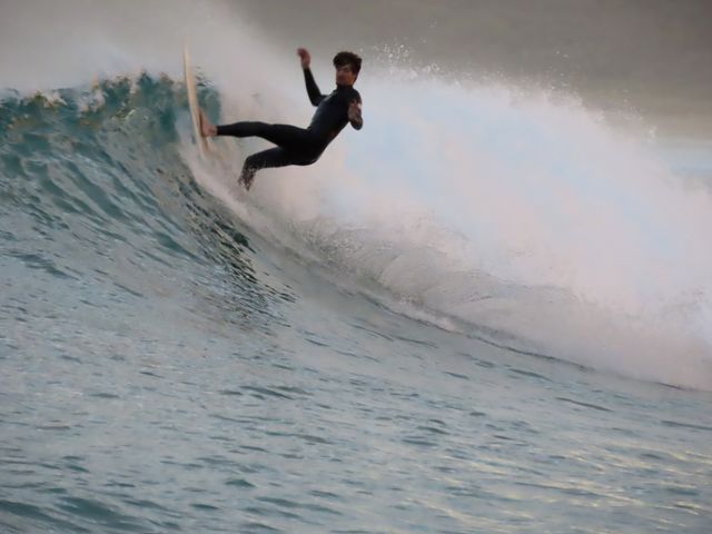 Summer by the ocean: surfer doing tricks up and down the wave at sunset on the Australian coast.