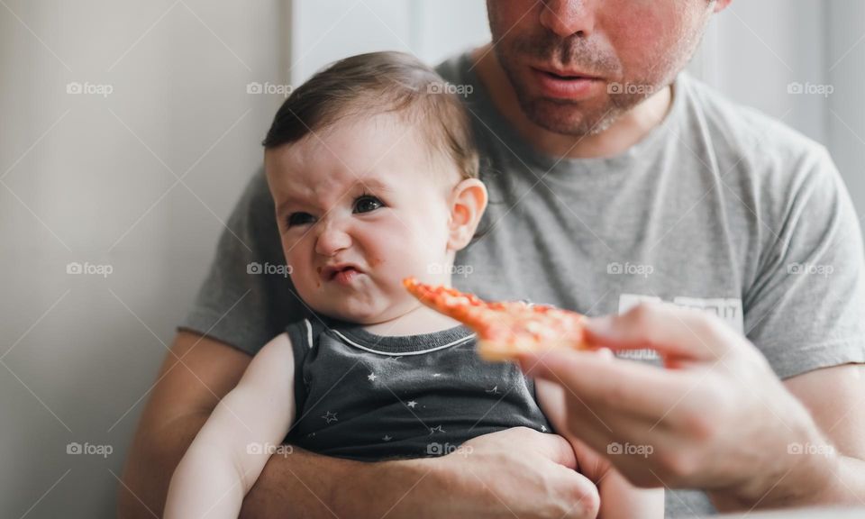 Portrait of a beautiful little caucasian girl sitting on her father's arms with disgust on her face turns her head away from a piece of homemade poultry in the hands of her father, close-up side view. Children emotion concept, lunch time,dads.