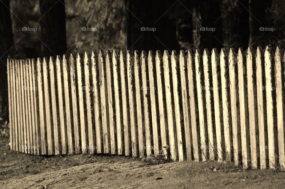A sepia-toned photo of a weather-worn picket fence at an old Japanese-Chinese cemetery. 
