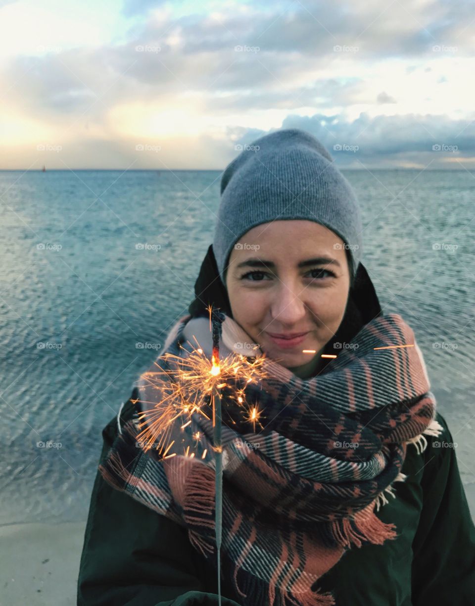 Happy woman holding fire cracker standing on beach
