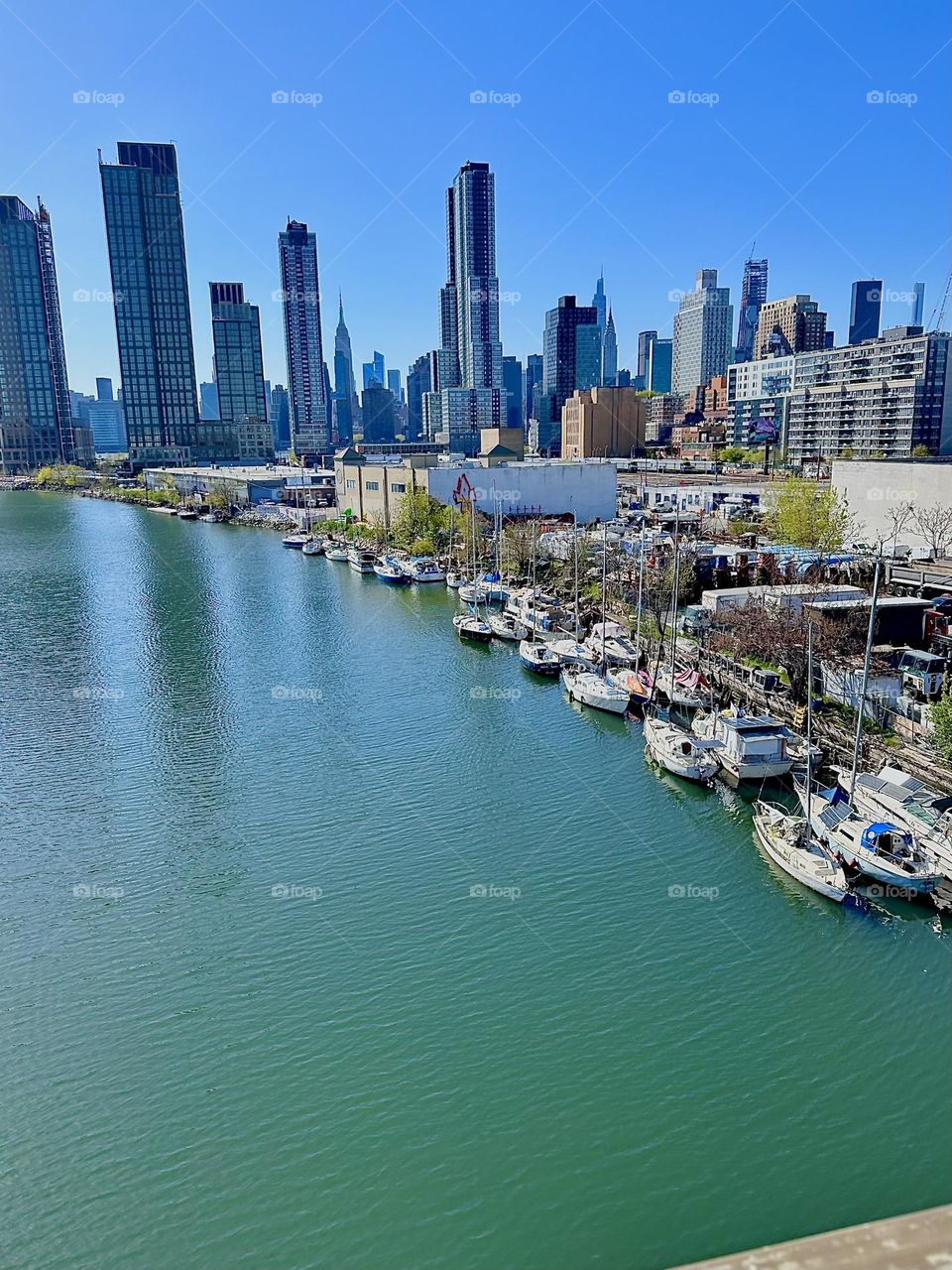 This is “Newtown Creek” with its great variety of boats seen from the “Pulaski Bridge” that connects LIC, Queens to “Greenpoint”, Bklyn. Across the “East River” we see “Manhattan” including the “Empire State Building”. 2024. Hypnotic Productions