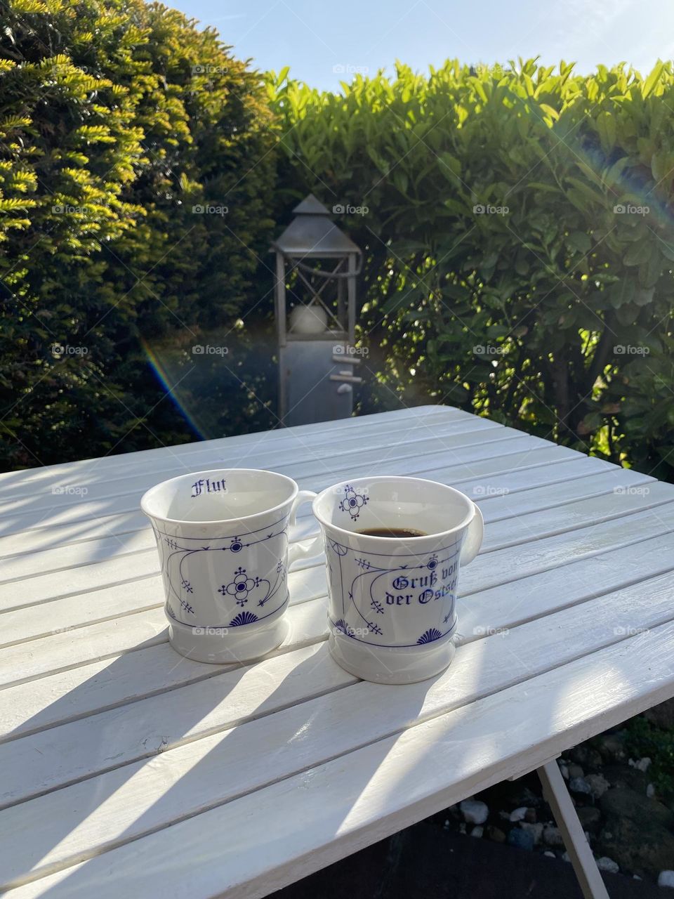 Sunrise behind the hedge, two cups of fresh coffee on the white wooden table in the morning at the Baltic Sea . A candle foarms the axis of the image