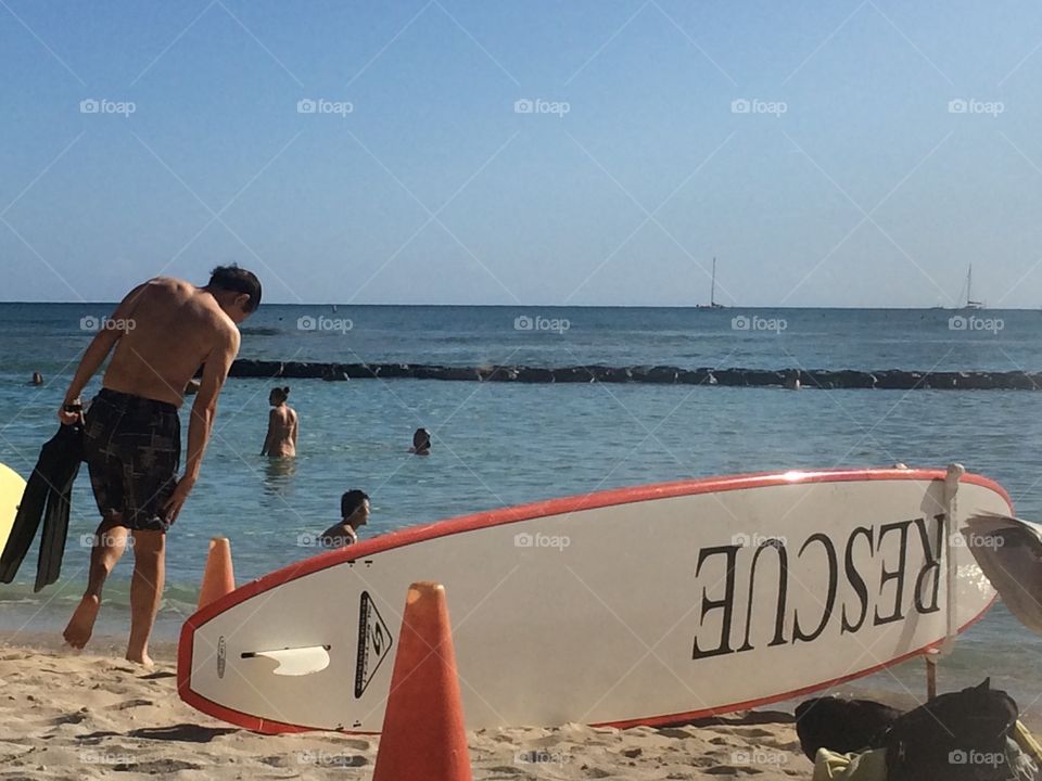 Lifeguard rescue surf board at the beach on the sand with people in the water and man walking on  shore 