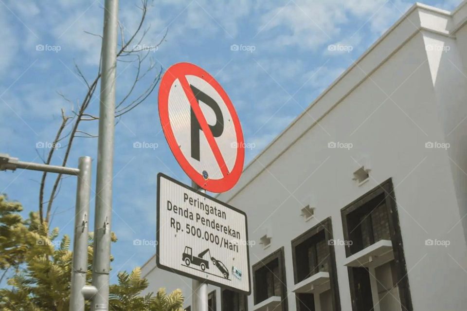 Close-up view of a no parking sign and an information board about fines for parking violations in front of a white building in low angle view