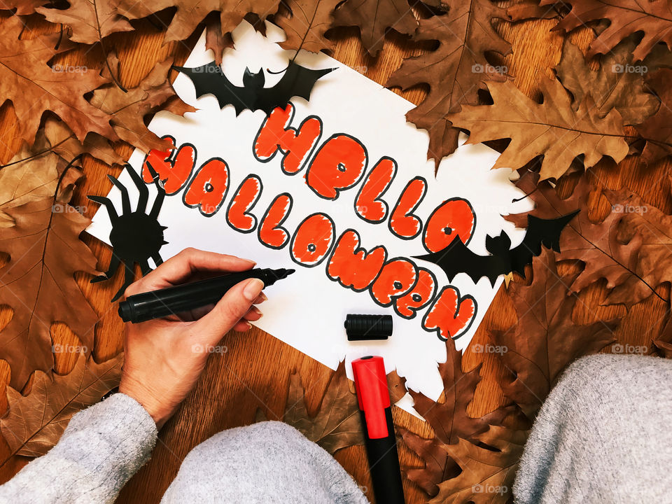 Drawing “Hello Halloween” on paper surrounded by dry fallen autumn leaves 