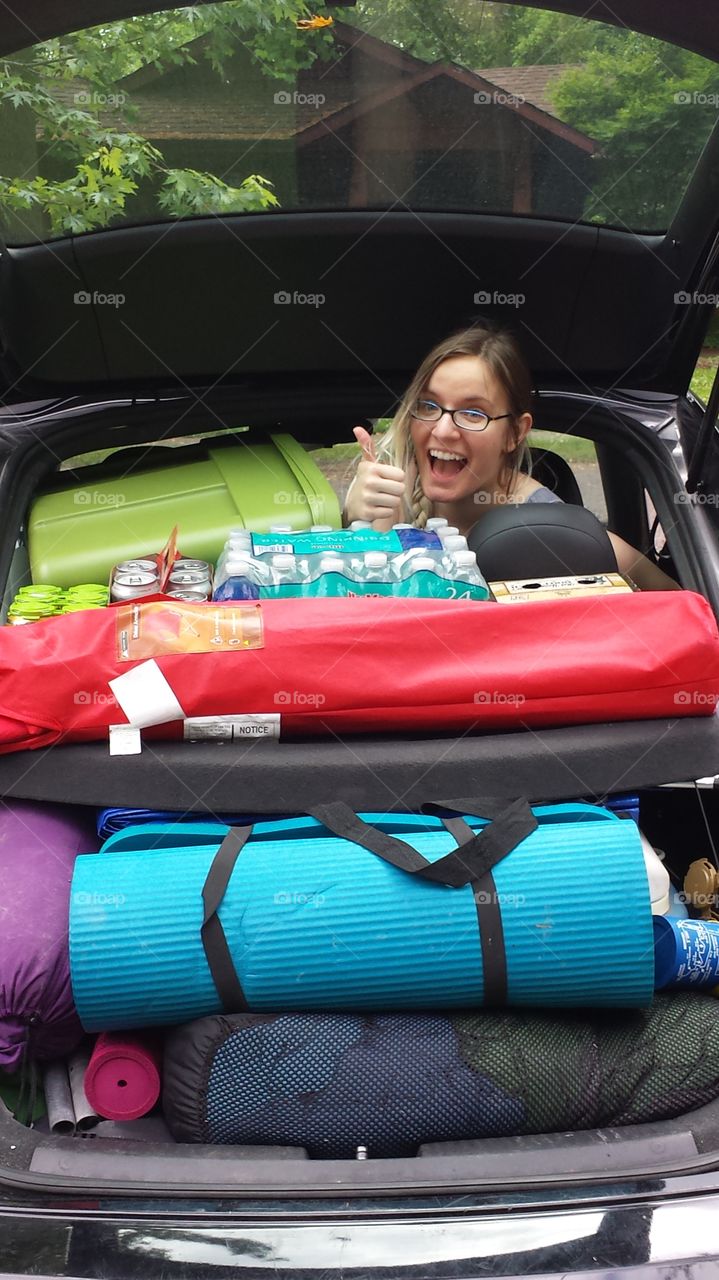 A woman giving a thumbs up in a car packed for a camping trip