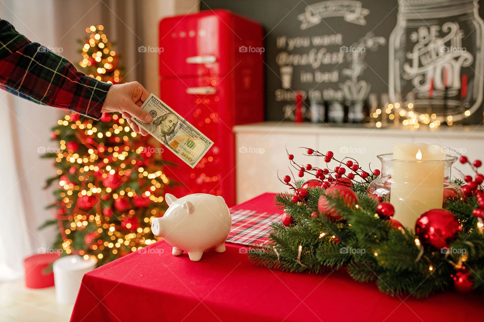 piggy bank with 100 dollars banknote in festive New Year atmosphere of scenery.  Magical bokeh with Christmas tree and bright lights.