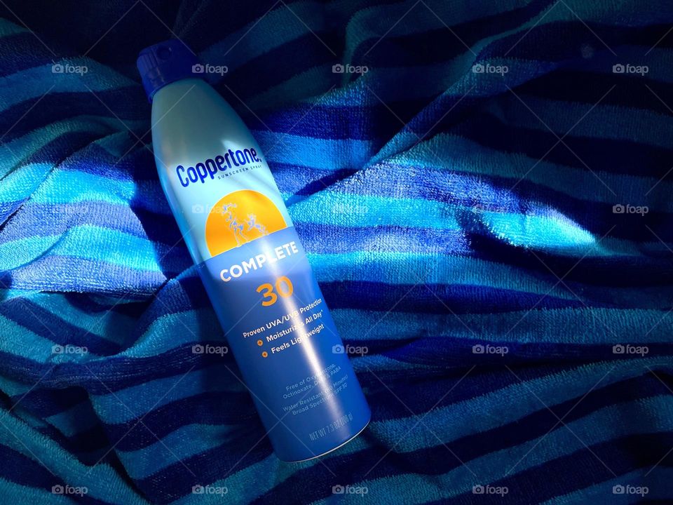 Sun protection spray  on the blue towel, top view 