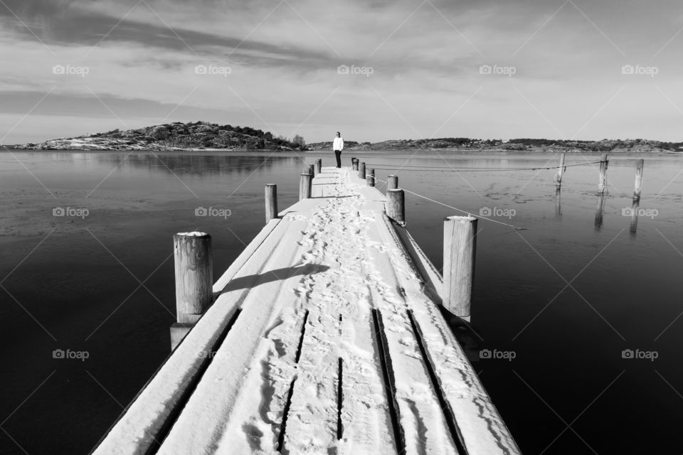 Man standing on snowy wooden pier in the frozen ocean 