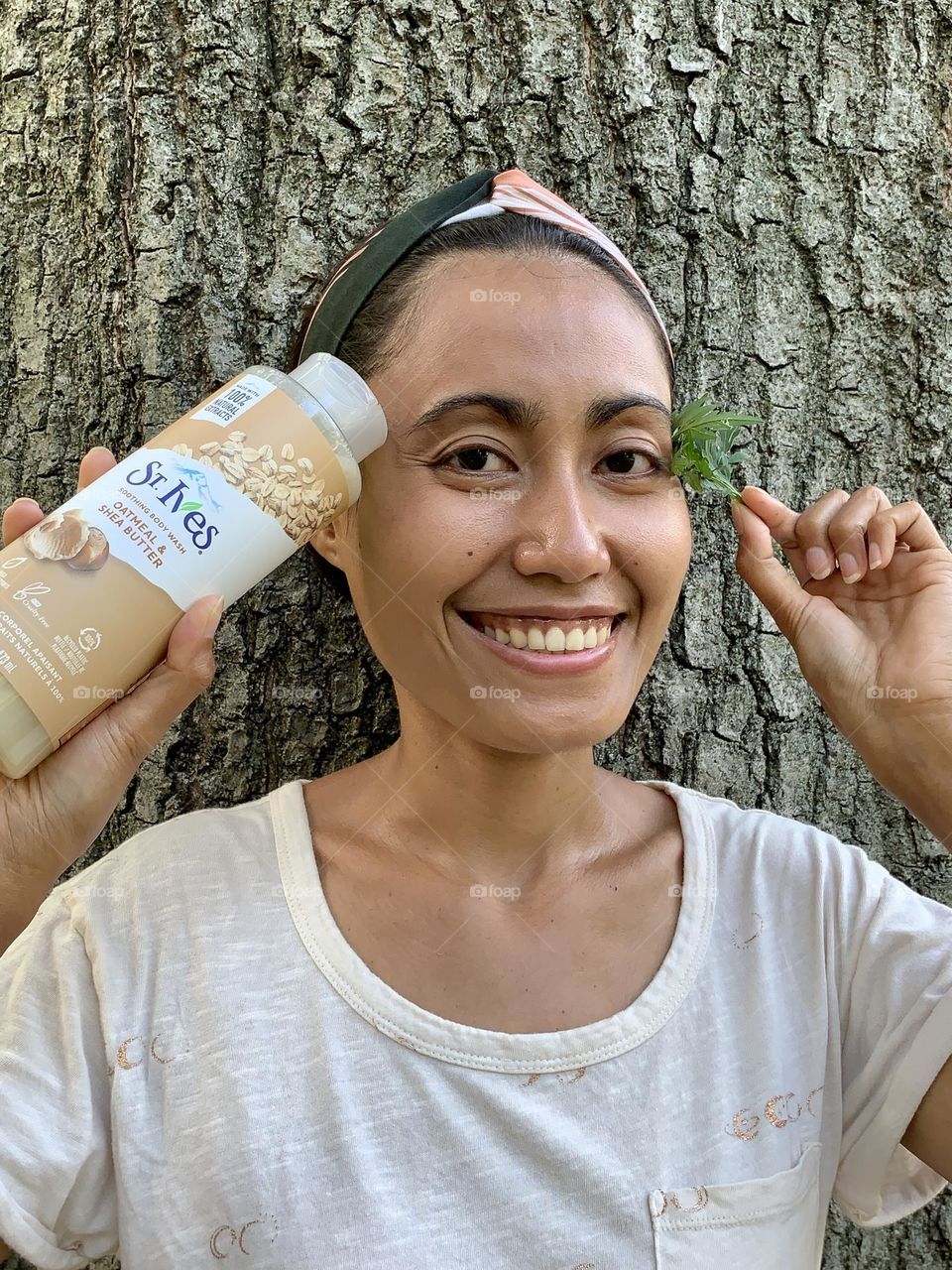 Energetic close up photo of a person holding St. Ives oatmeal shea butter soothing body wash against a big tree. 