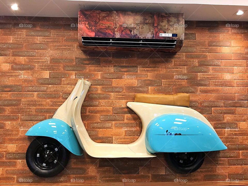 Blue and whiter scooter, Vespa brand, on the brick wall with colorful air conditioning 