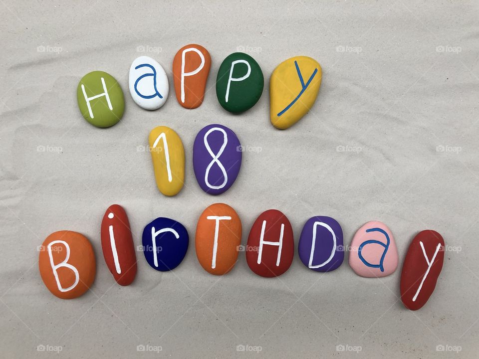 Happy 18 Birthday text with multi colored stones over white sand