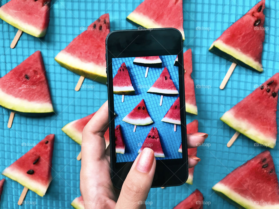 Female hand taking a photo of a red ripe watermelon slices 