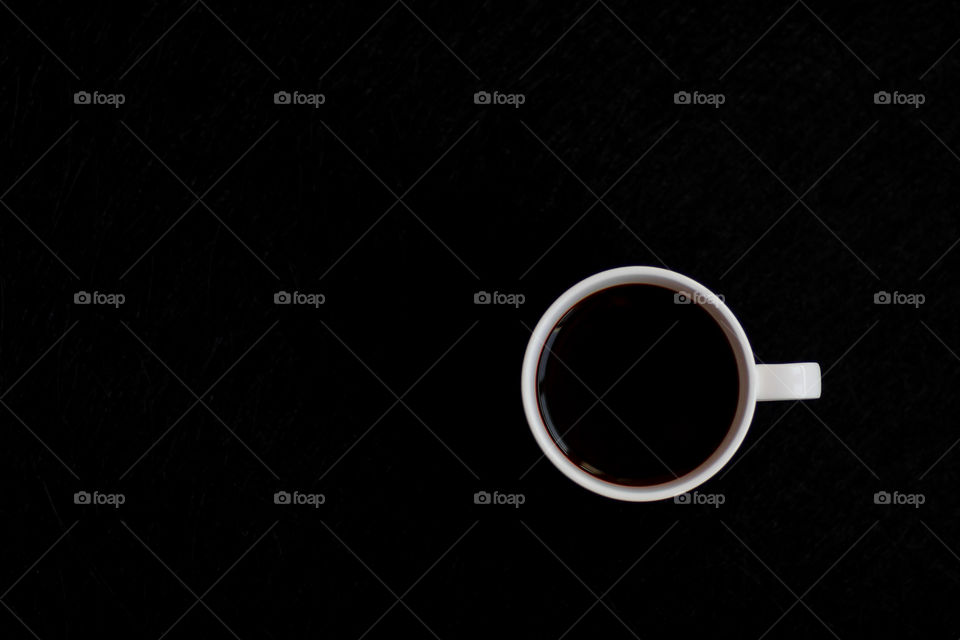 Top view to white cup with black coffee to the black background. Copy space.