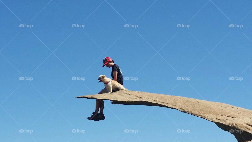 Girl and dog sitting on top of rock