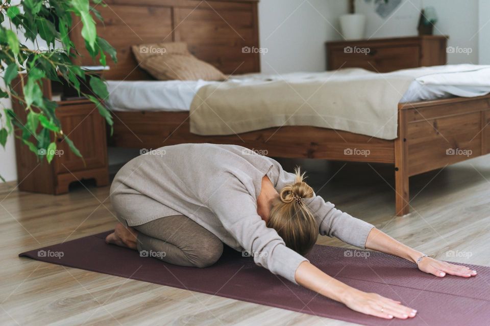 Beautiful blonde young woman in comfortable sport wear practice yoga in cozy bedroom at home