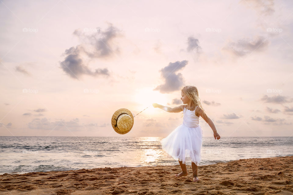 Cute little girl with blonde hair in white tutu dress on the beach 
