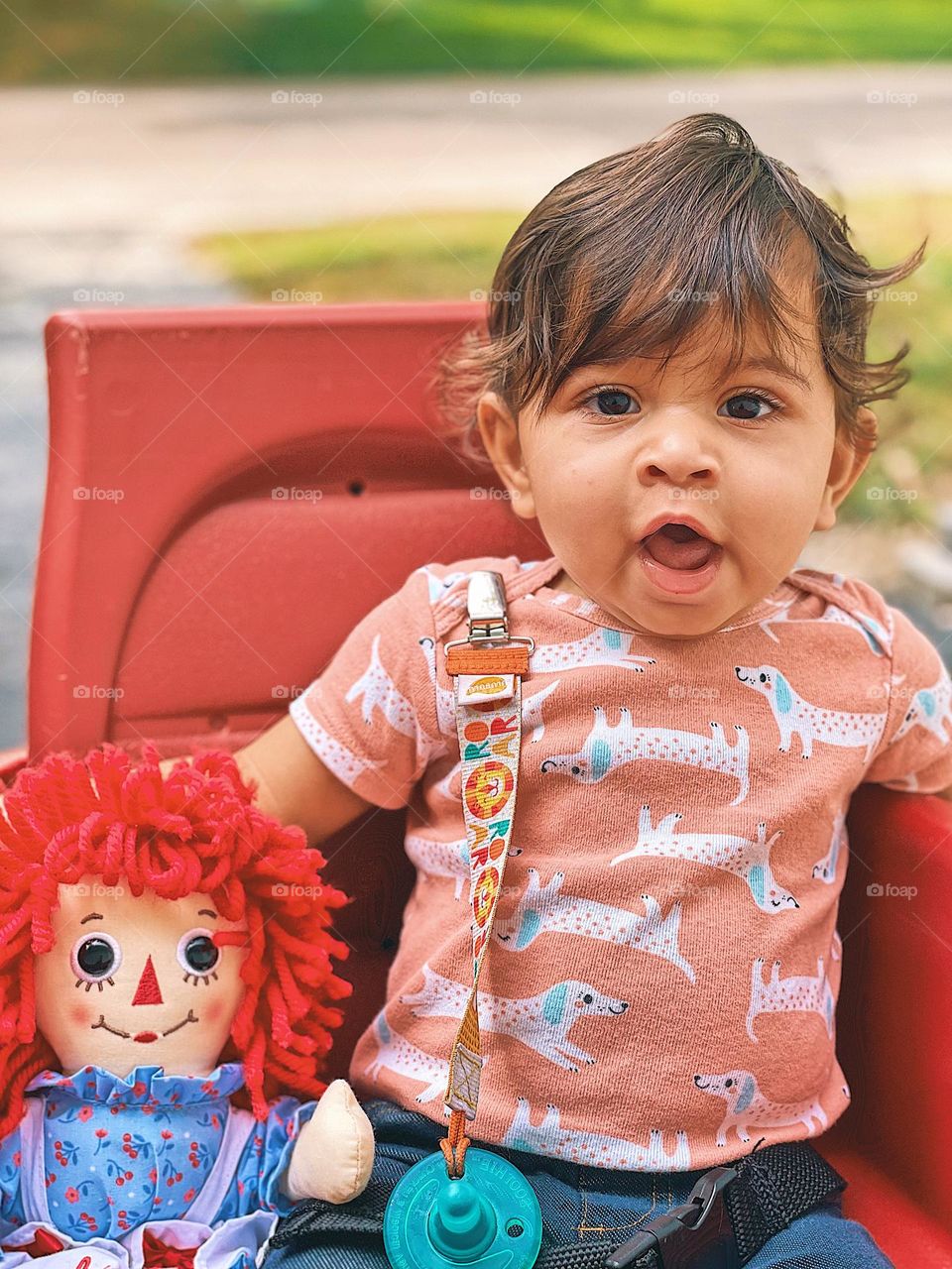 Baby girl goes for a wagon ride with Raggedy Ann doll, cute baby goes for a wagon ride, Raggedy Ann doll with baby girl, posing for a picture, smartphone portrait photography, going for a walk with the wagon