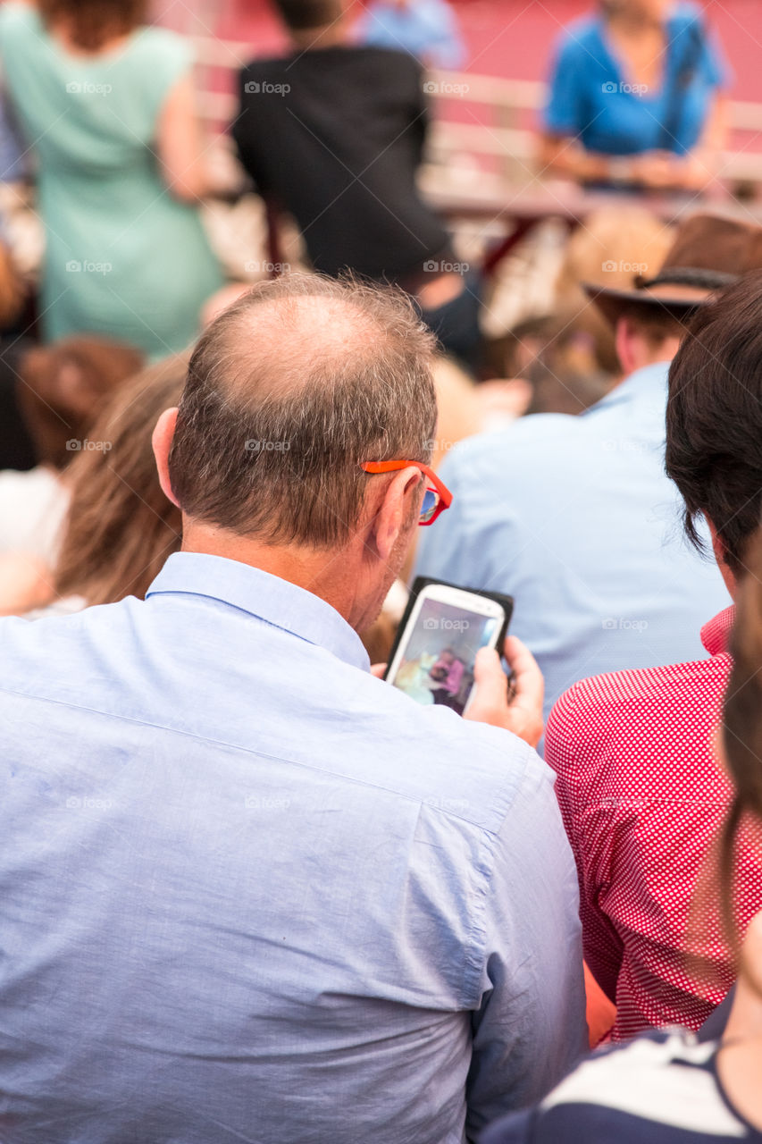 Senior Man Using His Smartphone At An Outdoor Concert
