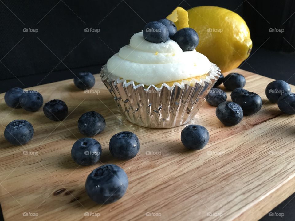 Blueberry lemon and cream cheese frosting cupcake with blueberries and lemon on bamboo background.