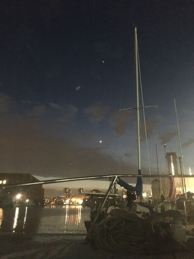 Aboard our sailboat, the “Salvation” late at night viewing the waters of the East River at Newtown Creek, Long Island City, Queens, New York and the illuminated cityscape in the far distance reflecting in it. Photo 2018. Hypnotic Productions