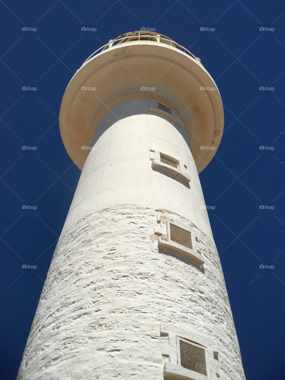 Old white stone lighthouse shot from ground up against a vivid blue sky