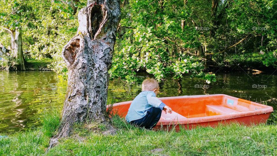 boy sitting besides rowboats by forest lake