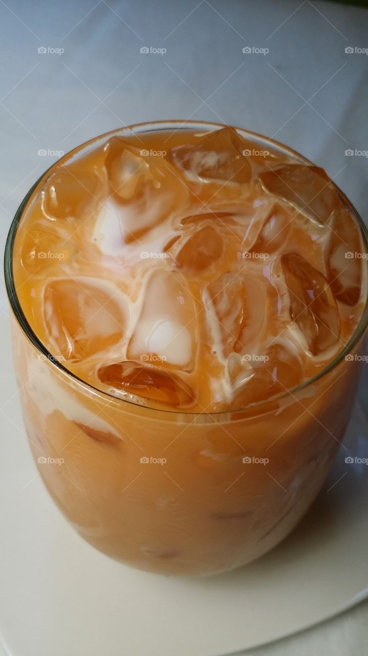 A glass of Sweet Thai Iced Tea topped with creamy milk