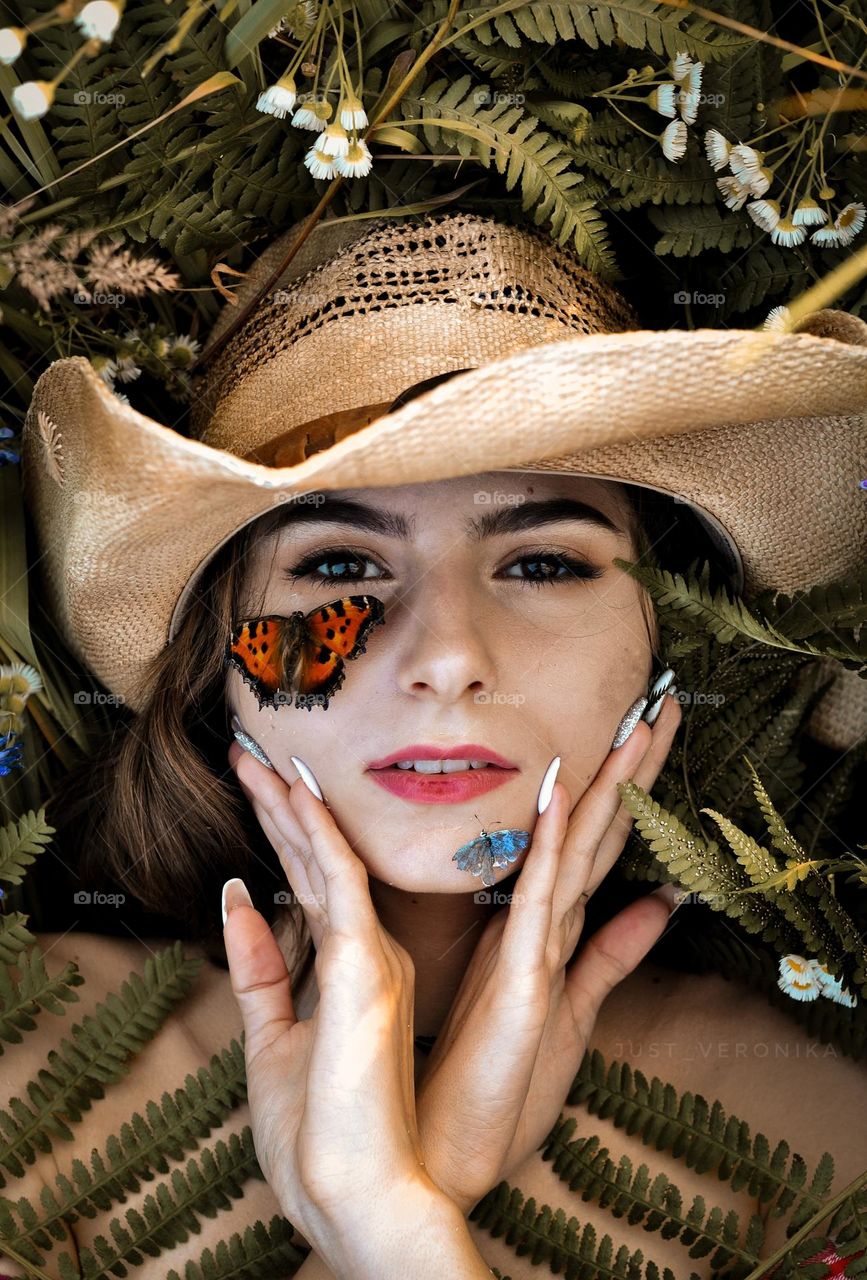 portrait of a girl in a cowboy hat lying in the grass with a butterfly on her face
