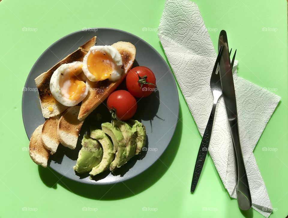 poached eggs, croutons, avocados, tomatoes served breakfast on a green background