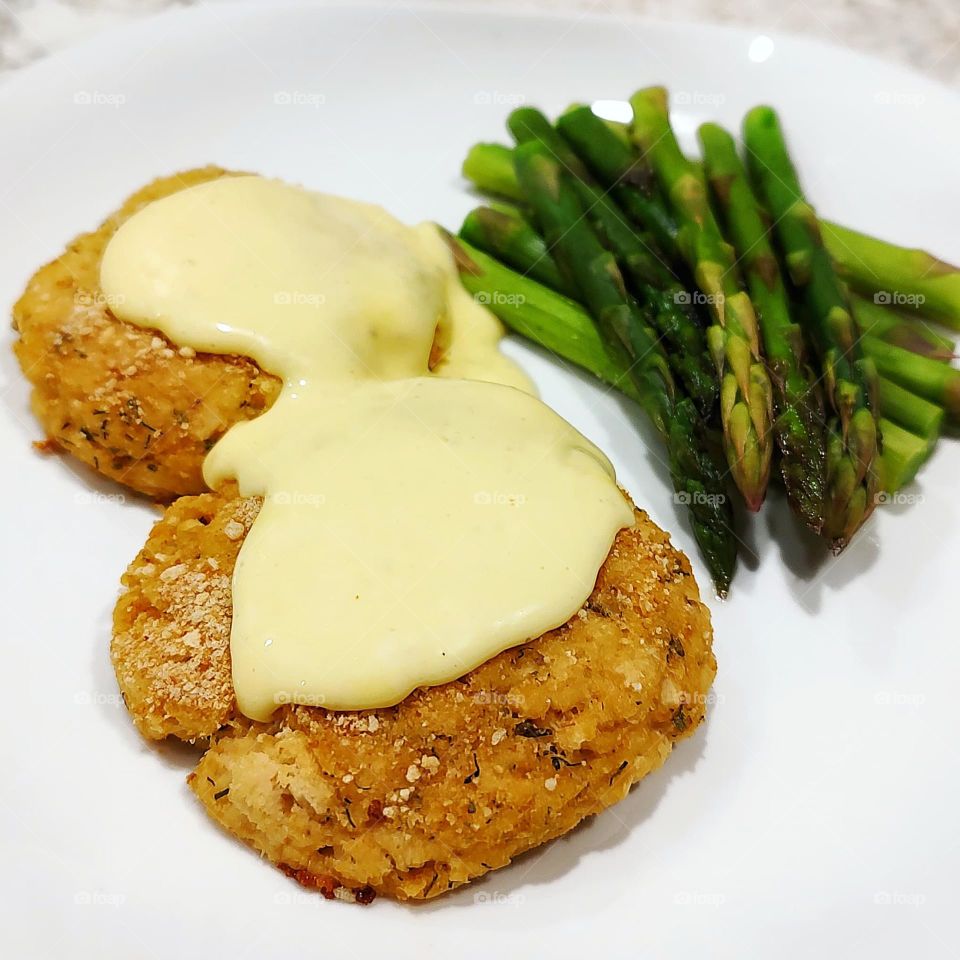 Homemade Crab Cakes topped with Hollandaise sauce and halved asparagus on a white plate