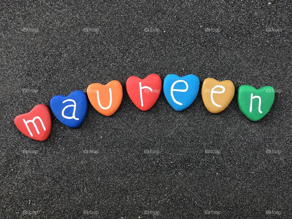 Maureen, feminine name with multicolored heart stones over black volcanic sand