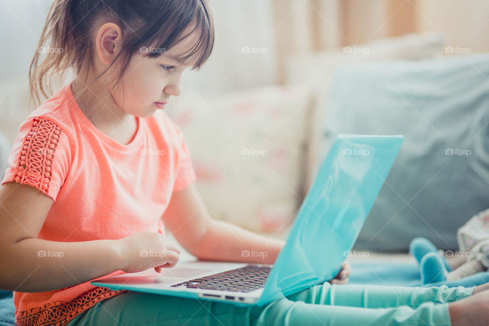 Little girl with gadgets(laptop and tablet) in the bed.