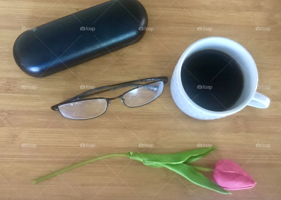 Cup of coffee in the morning with a pink tulip and reading glasses on a wooden table 