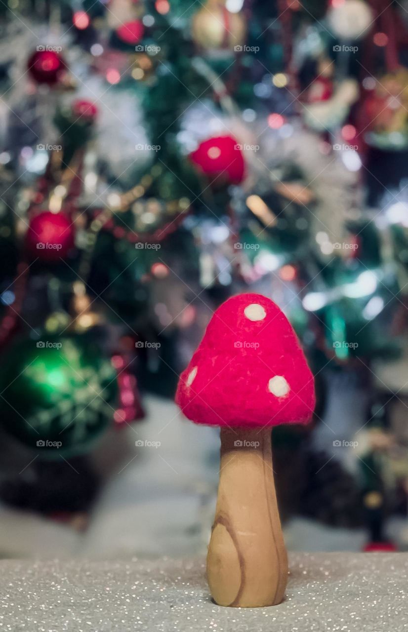 A red & white toadstool made from wood & felt stands in front of a decorated Christmas tree