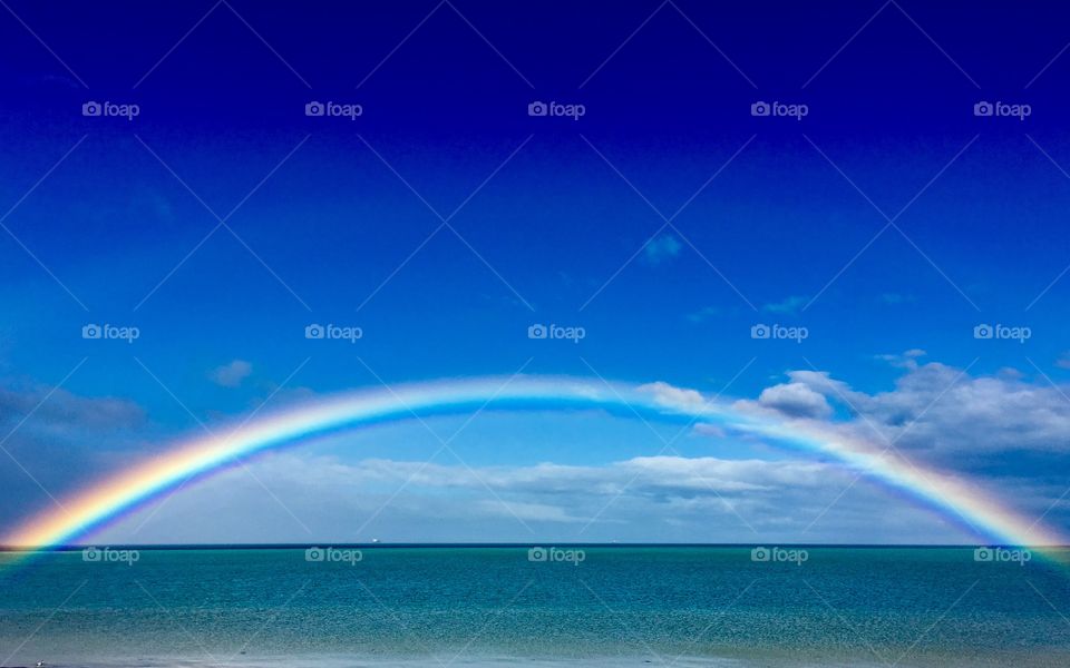 Full colourful  rainbow with faint double arching and stretching over the ocean horizon and through the aquamarine turquoise blue water, on brilliantly sunny blue sky and light cloudy day, South Australia, Spencer Gulf Eyre Peninsula