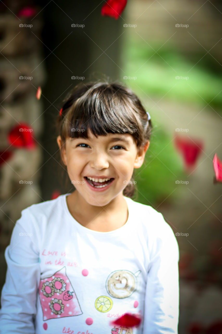 Happy girl with red rose petals in the air