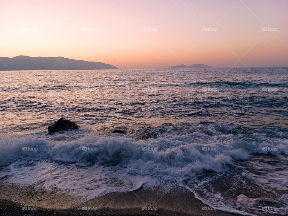 Sea with waves against the backdrop of a beautiful sunset and mountains
