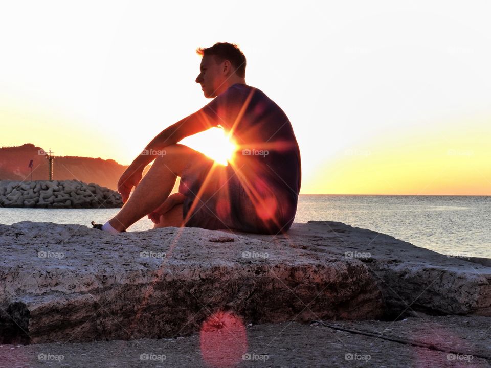 A man sits on the seashore at sunset