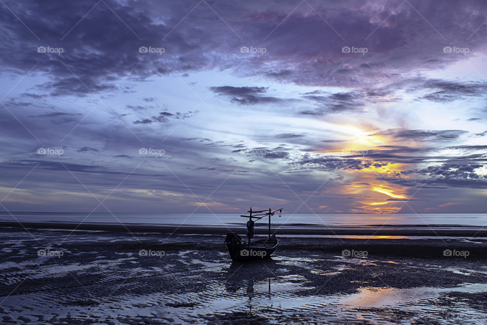 The morning sun light in the sea and the boat on the beach.