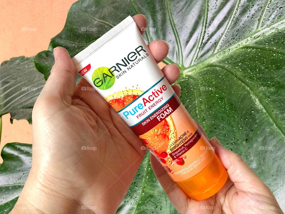Hand holding tube of Garnier facial cleanser; pure active fruit energy for acne treatment and skin brightening 