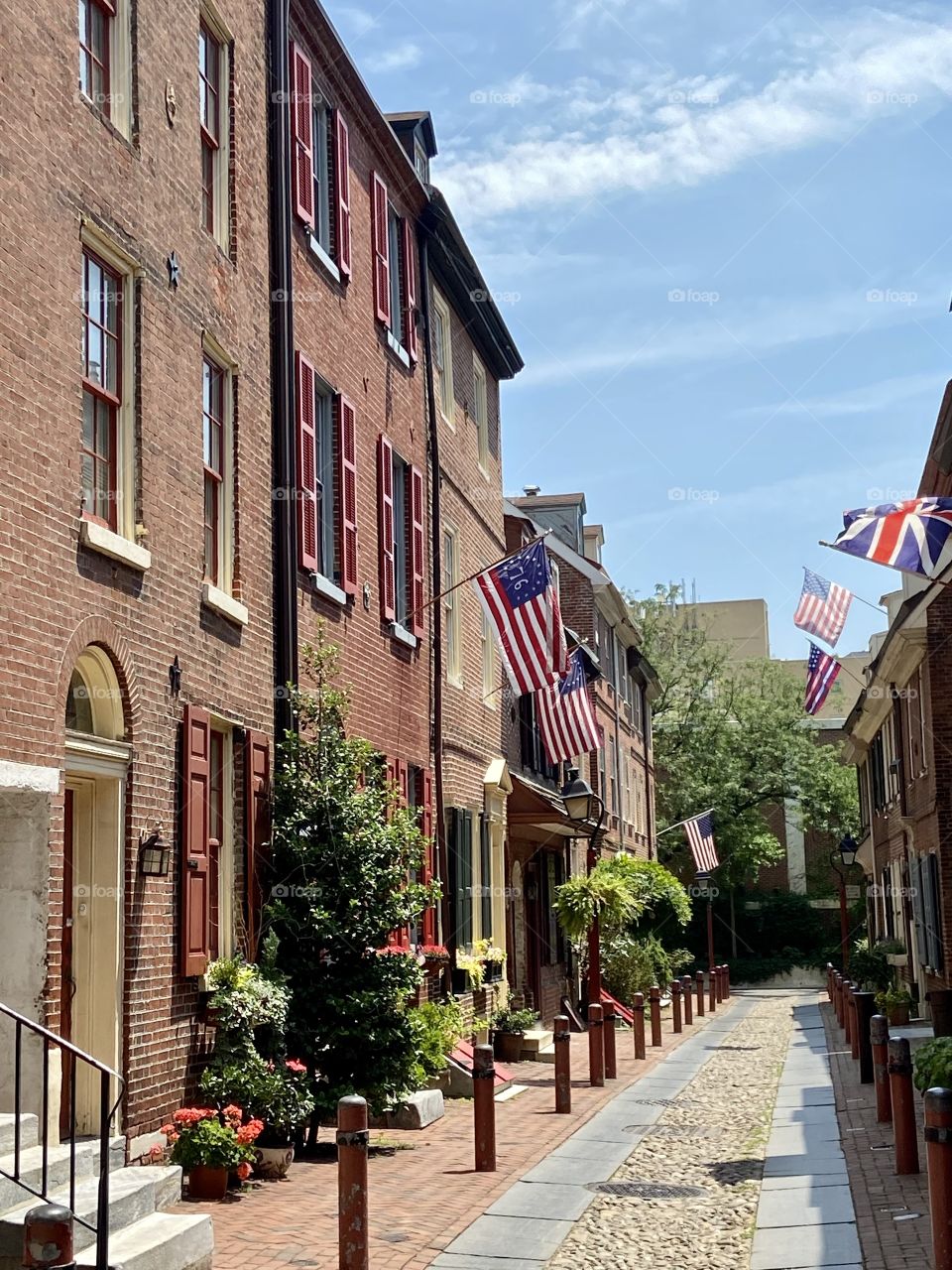 A series of brick row houses on a cobblestone street with pretty landscaping and American flags waving