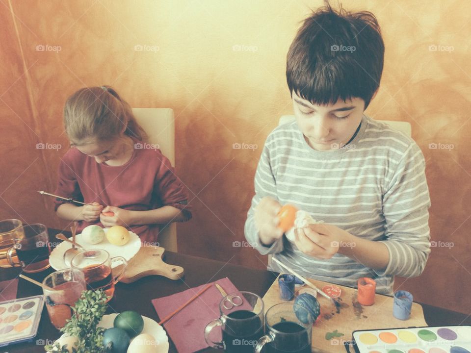 Brother and sister painting Easter eggs at home