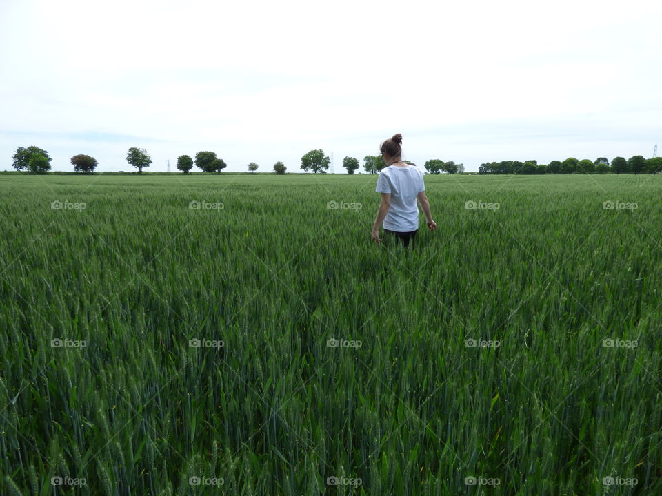 a young woman walking away into the rye field deep in thought wearing white t-shirt in a warm spring afternoon