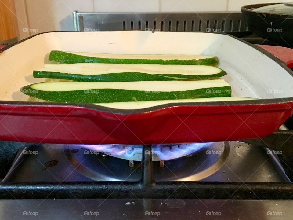 Zucchini sliced lengthwise on griddle on gas stove closeup 