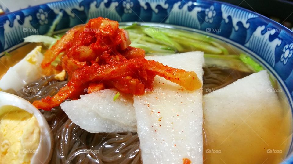 Cold soba soup noodle meal, with fresh boiled egg, sliced cucumber, white radish topped with some kimchi (fermented vegetable).