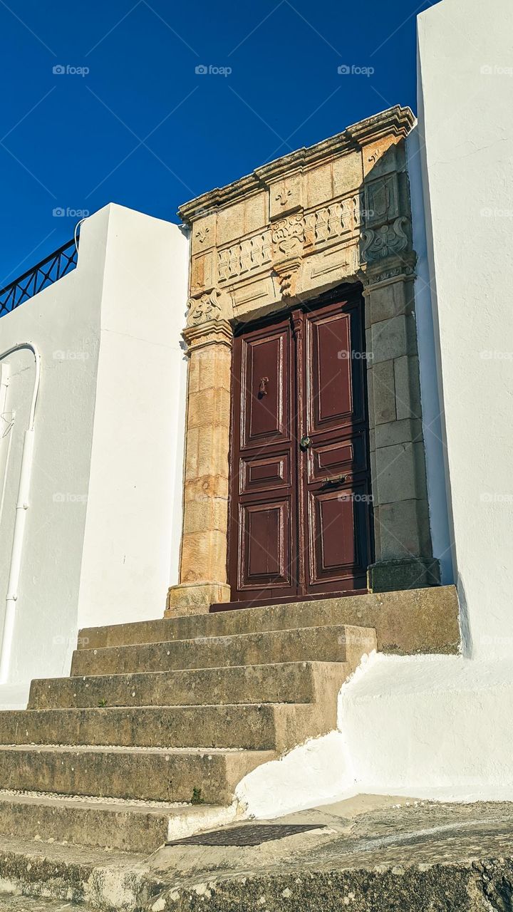 Beautiful view of a Greek-style house with brown doors and a staircase with rectangular cayenne steps, close-up view from below.