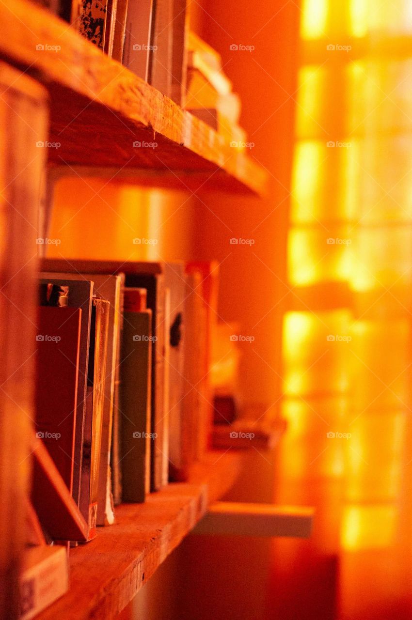 Photo of books illuminated by sunlight through an orange curtain.
