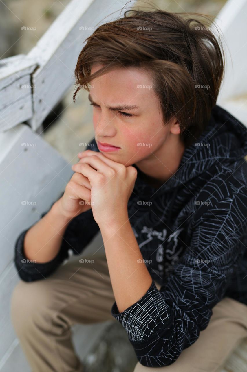 a thirteen-year-old teenager, sitting looking into the distance, a boy sitting by the sea, a handsome, mature boy